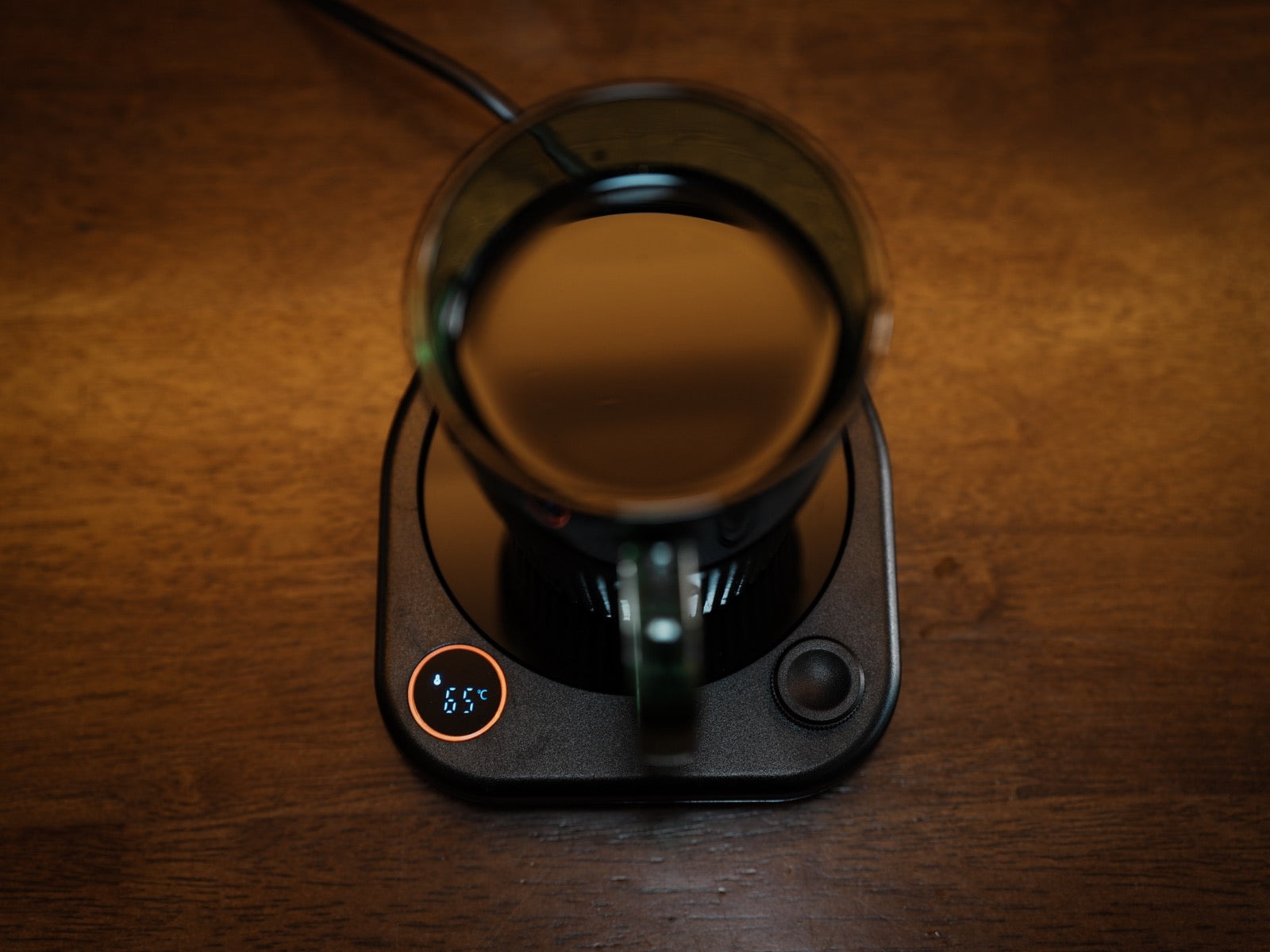 Actual CT-01 on a wooden table, warming a glass mug of coffee